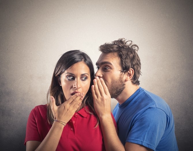 man whispering a secret into ear of shocked woman